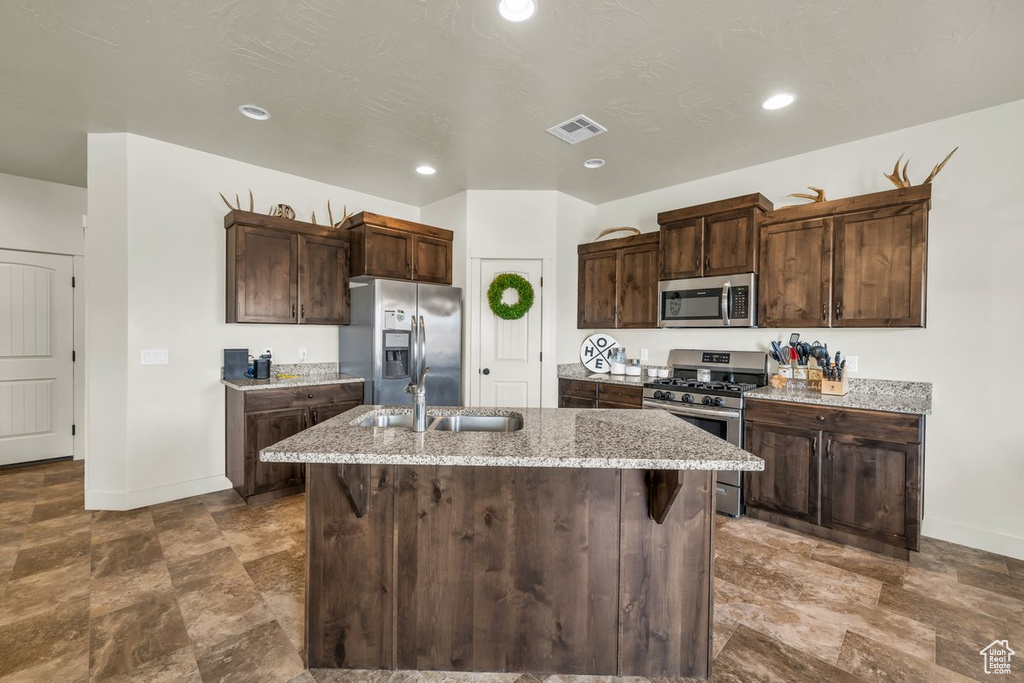 Kitchen with appliances with stainless steel finishes, light stone countertops, sink, and a center island with sink
