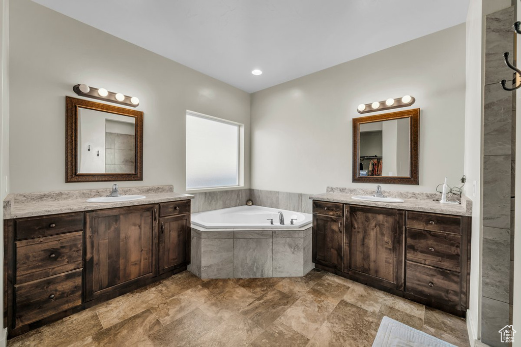 Bathroom featuring tiled bath, dual vanity, and tile flooring