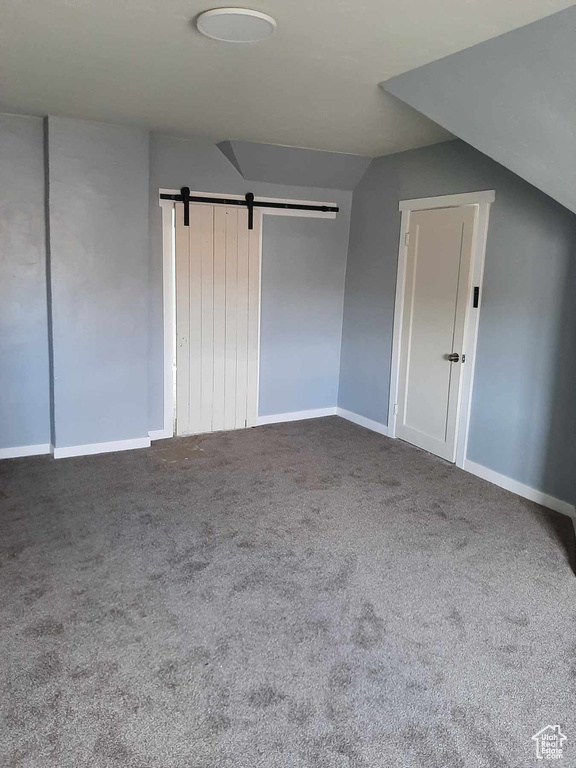 Unfurnished bedroom featuring dark colored carpet, a barn door, and vaulted ceiling