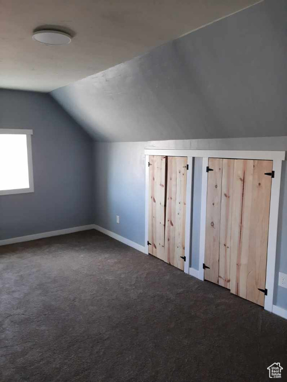 Additional living space featuring dark carpet and vaulted ceiling