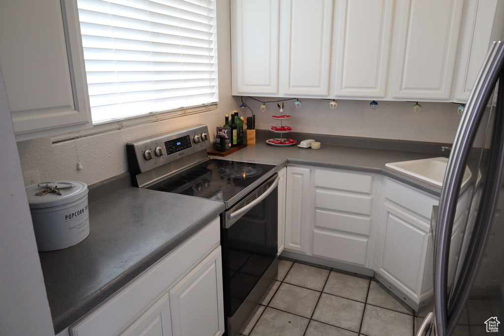 Kitchen featuring stainless steel range with electric stovetop, white cabinets, black fridge, and light tile flooring