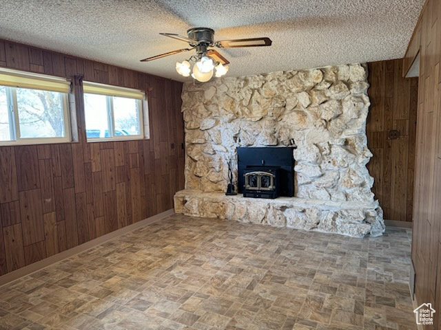Unfurnished living room with wood walls, ceiling fan, a wood stove, and a fireplace