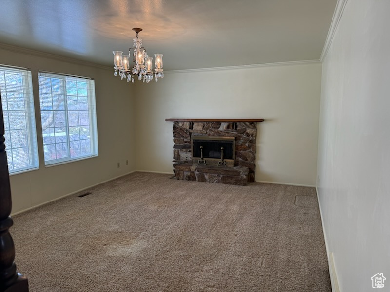 Unfurnished living room with an inviting chandelier, a stone fireplace, carpet flooring, and crown molding