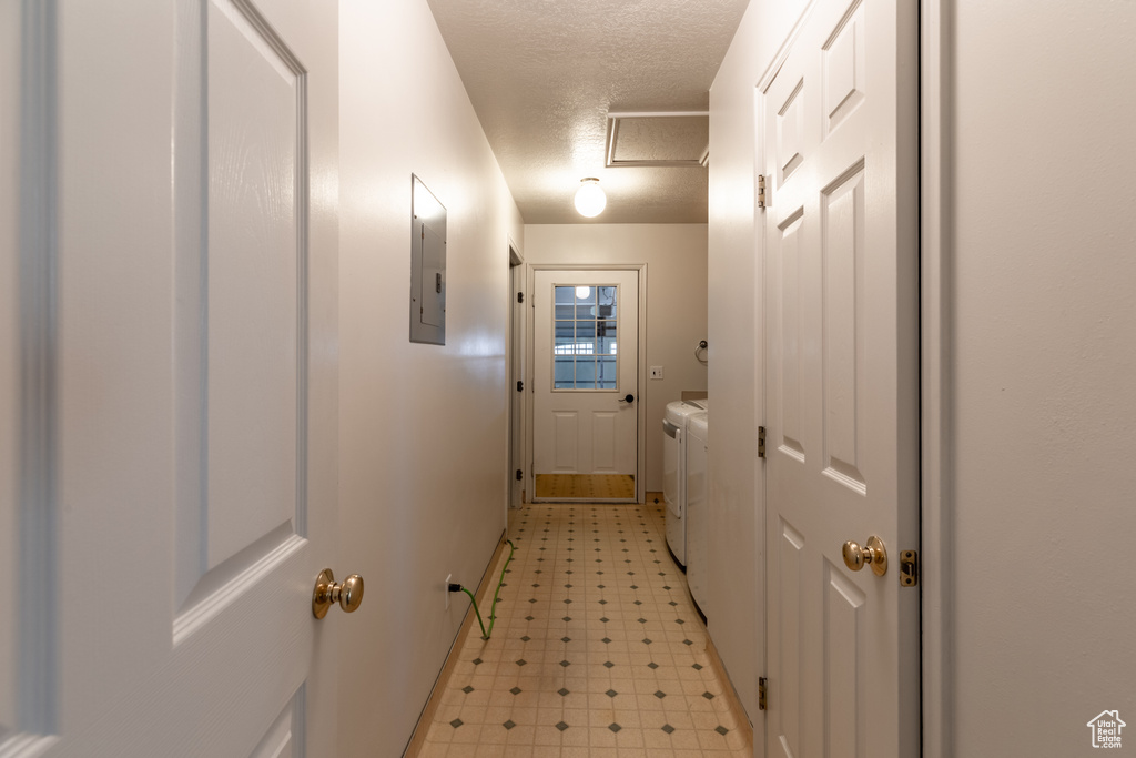 Hall with light tile flooring, washer and dryer, and a textured ceiling