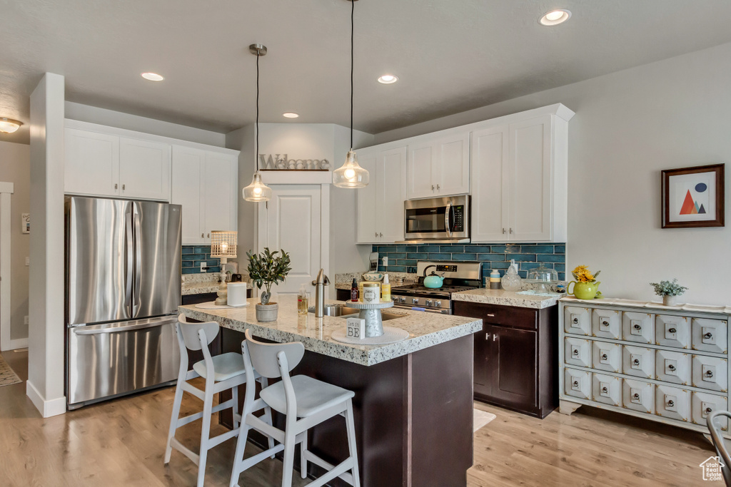 Kitchen with appliances with stainless steel finishes, light hardwood / wood-style flooring, and tasteful backsplash