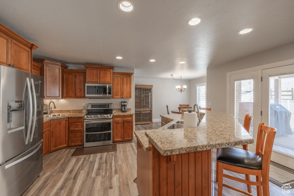 Kitchen with appliances with stainless steel finishes, a breakfast bar area, a notable chandelier, light hardwood / wood-style flooring, and sink