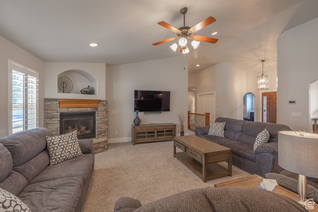 Carpeted living room featuring a stone fireplace and ceiling fan with notable chandelier