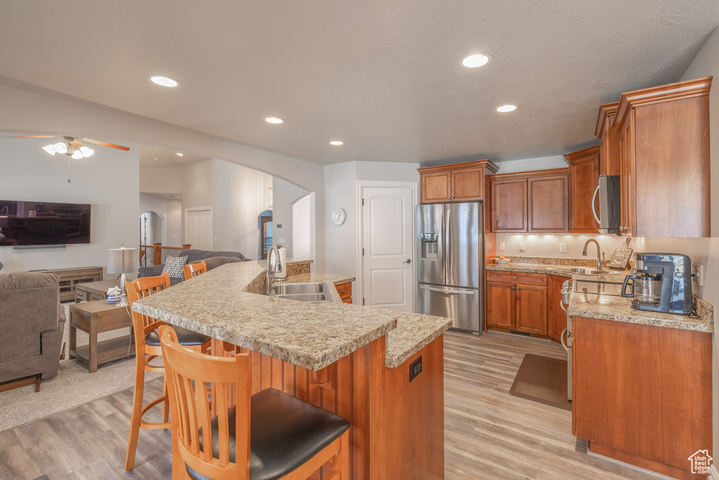 Kitchen with light hardwood / wood-style floors, appliances with stainless steel finishes, ceiling fan, and a kitchen bar