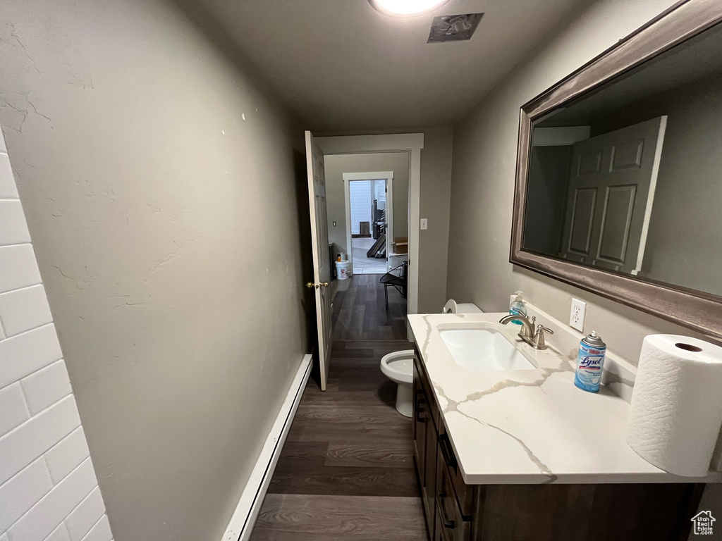 Bathroom with a baseboard radiator, vanity, toilet, and hardwood / wood-style flooring