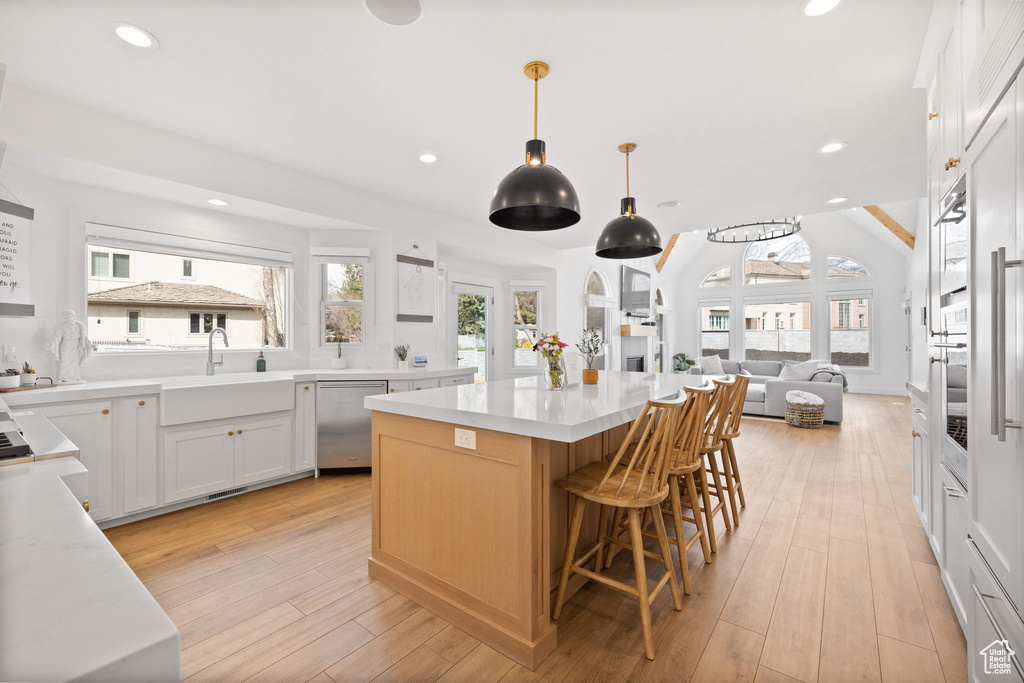 Kitchen with light hardwood / wood-style floors, a kitchen island, dishwasher, and white cabinetry