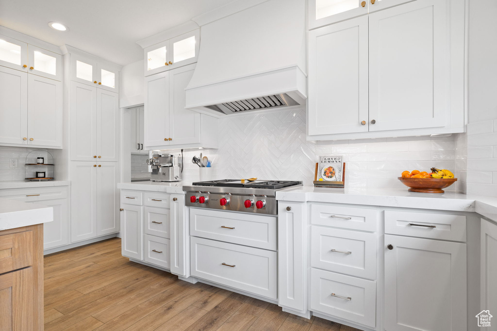Kitchen featuring backsplash, premium range hood, light wood-type flooring, and white cabinetry