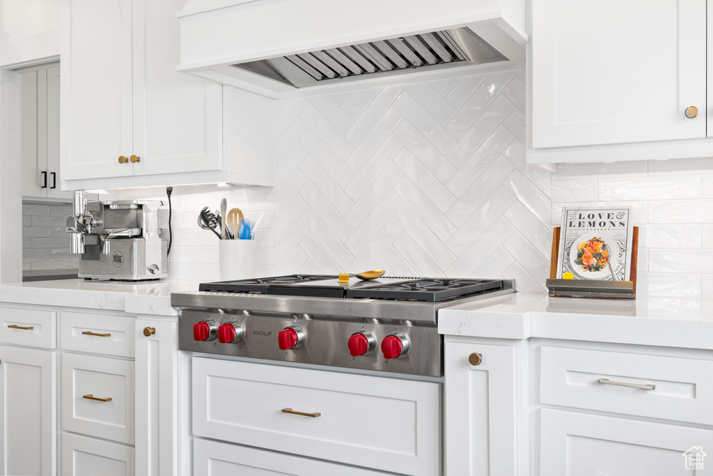 Kitchen featuring backsplash, white cabinetry, and custom range hood