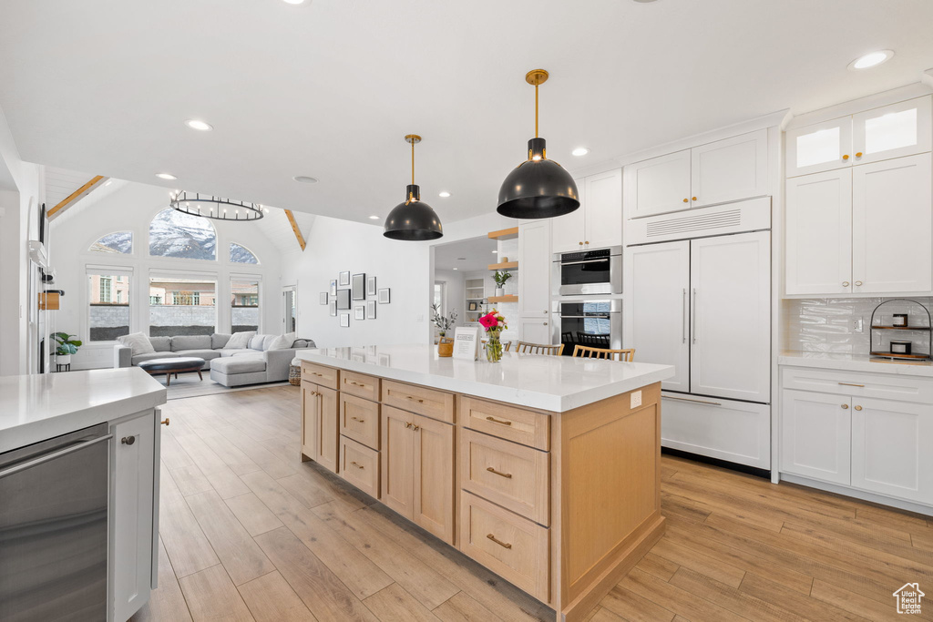 Kitchen with decorative light fixtures, light hardwood / wood-style floors, paneled built in fridge, light brown cabinetry, and backsplash