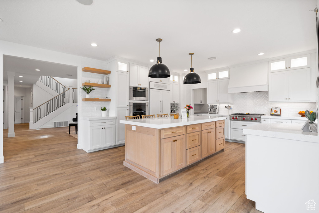 Kitchen featuring light brown cabinets, white cabinets, stainless steel appliances, light wood-type flooring, and a center island
