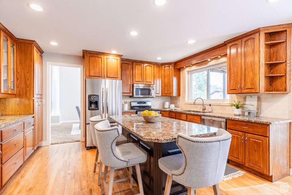 Kitchen with appliances with stainless steel finishes, light stone counters, a kitchen island, and light hardwood / wood-style floors