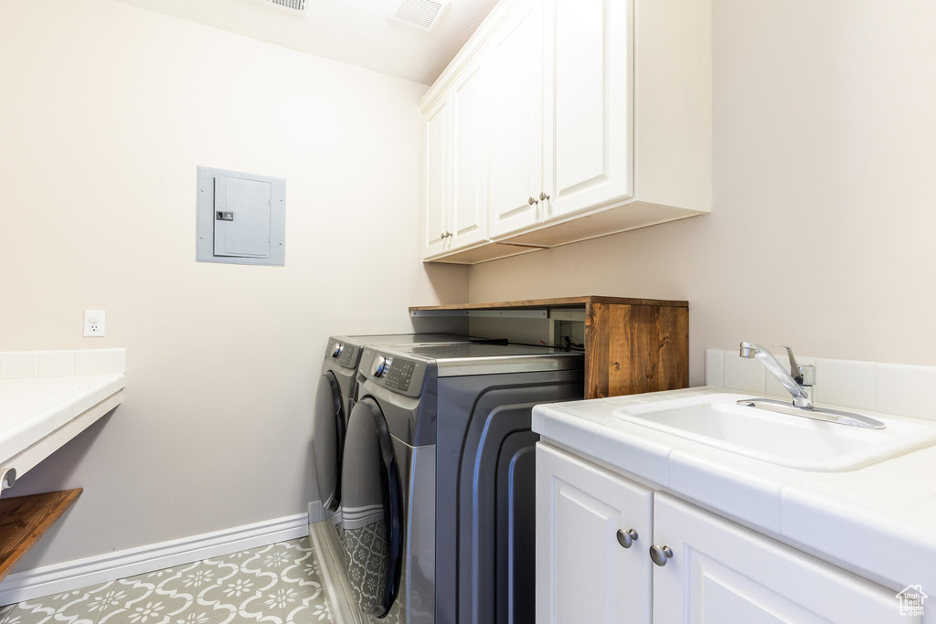 Clothes washing area featuring washer hookup, sink, light tile floors, cabinets, and washer and dryer
