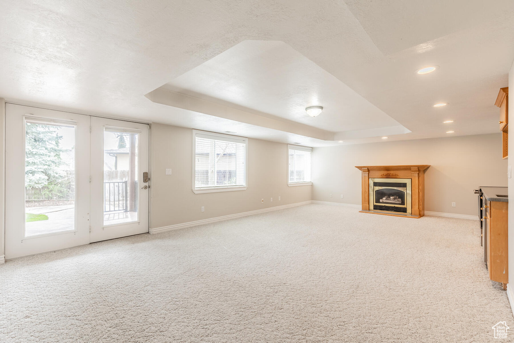 Unfurnished living room featuring a wealth of natural light, light carpet, and a raised ceiling
