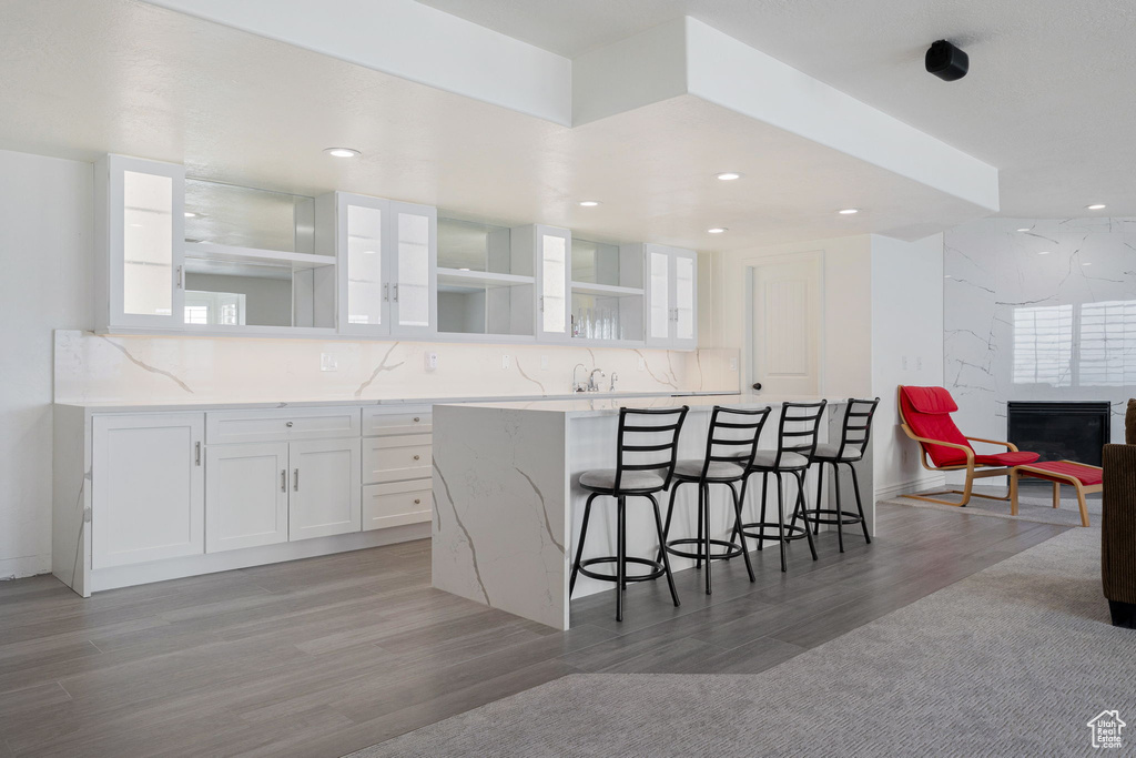 Kitchen with light stone counters, tasteful backsplash, white cabinets, a kitchen bar, and light hardwood / wood-style flooring