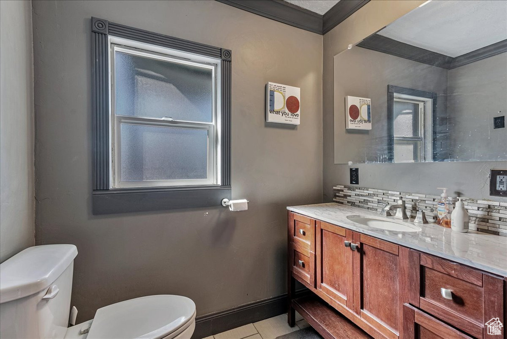 Bathroom featuring vanity, backsplash, tile floors, toilet, and crown molding