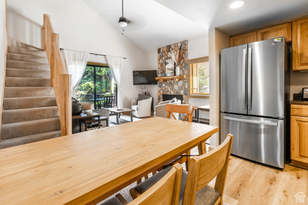 Kitchen featuring stainless steel fridge, ceiling fan, light wood-type flooring, a fireplace, and lofted ceiling