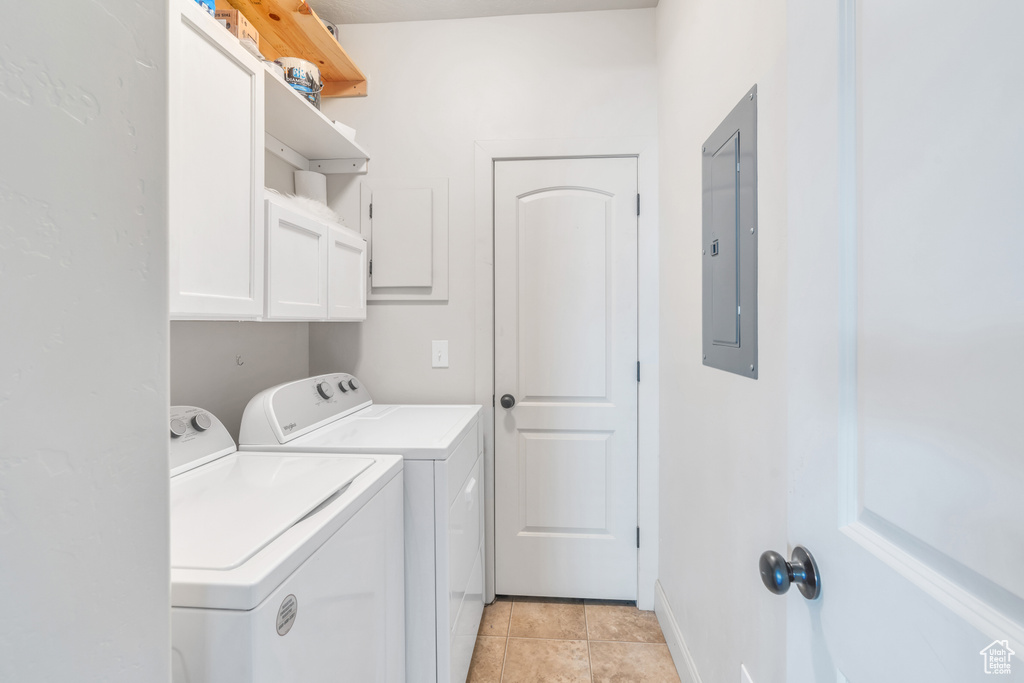 Washroom featuring separate washer and dryer, light tile floors, and cabinets