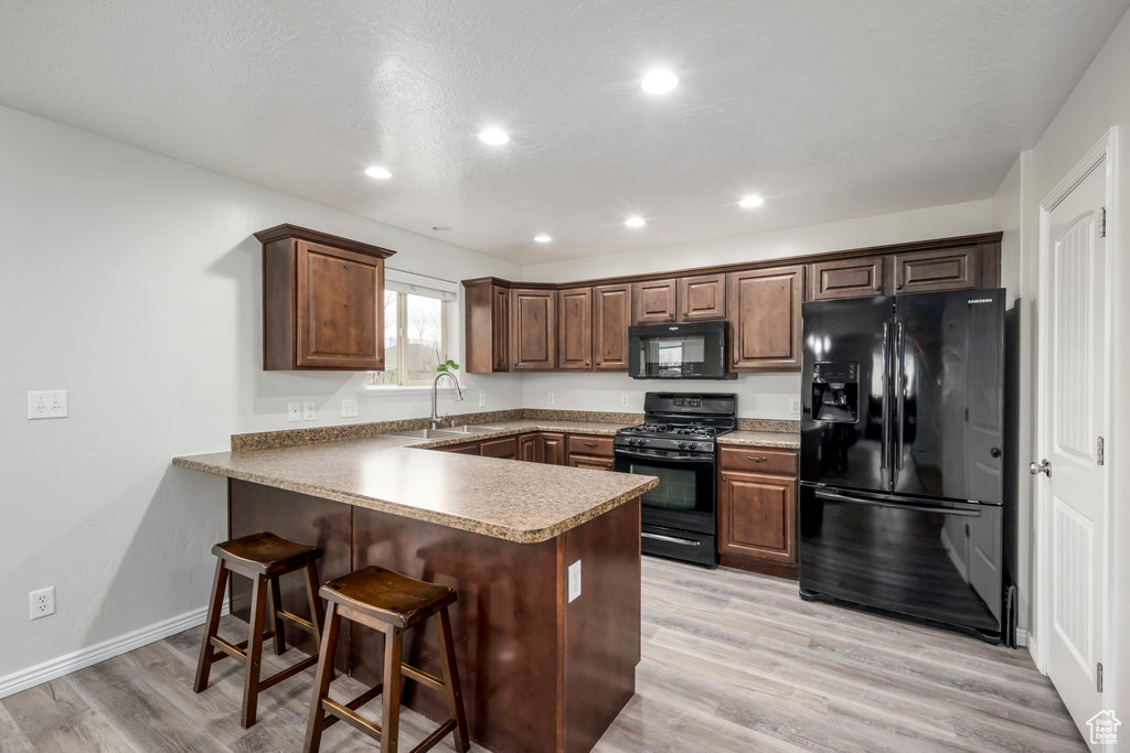 Kitchen featuring kitchen peninsula, black appliances, a breakfast bar, sink, and light hardwood / wood-style flooring
