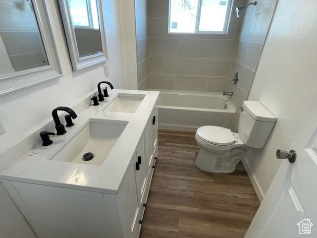 Full bathroom with wood-type flooring, vanity with extensive cabinet space, toilet, and tiled shower / bath