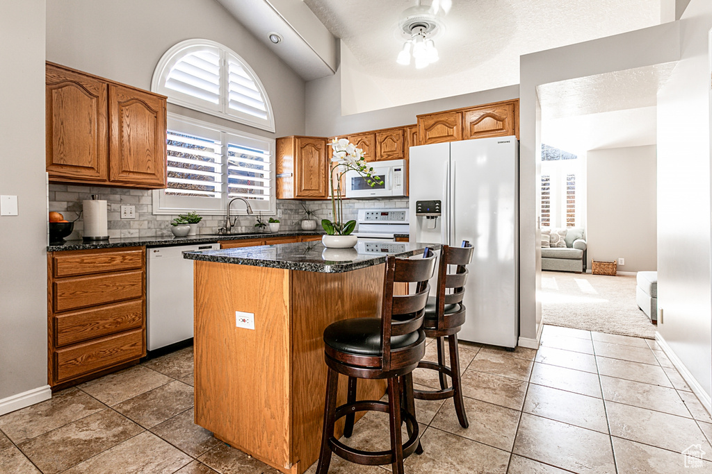 Kitchen featuring a kitchen island, ceiling fan, a breakfast bar, white appliances, and backsplash