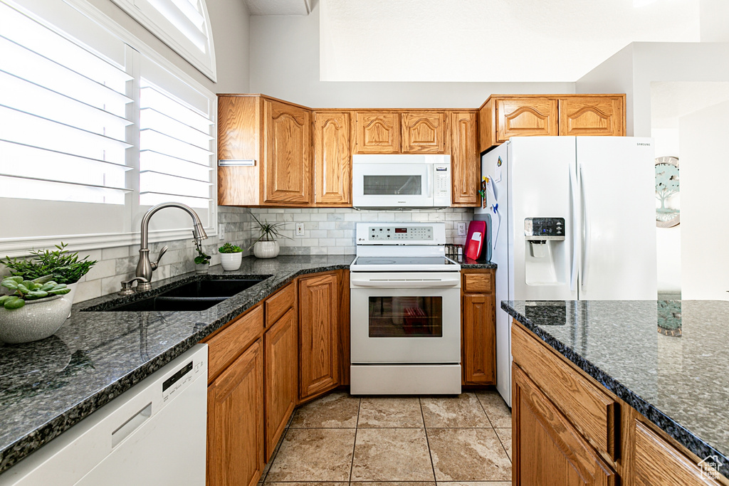 Kitchen featuring white appliances, backsplash, dark stone countertops, and sink