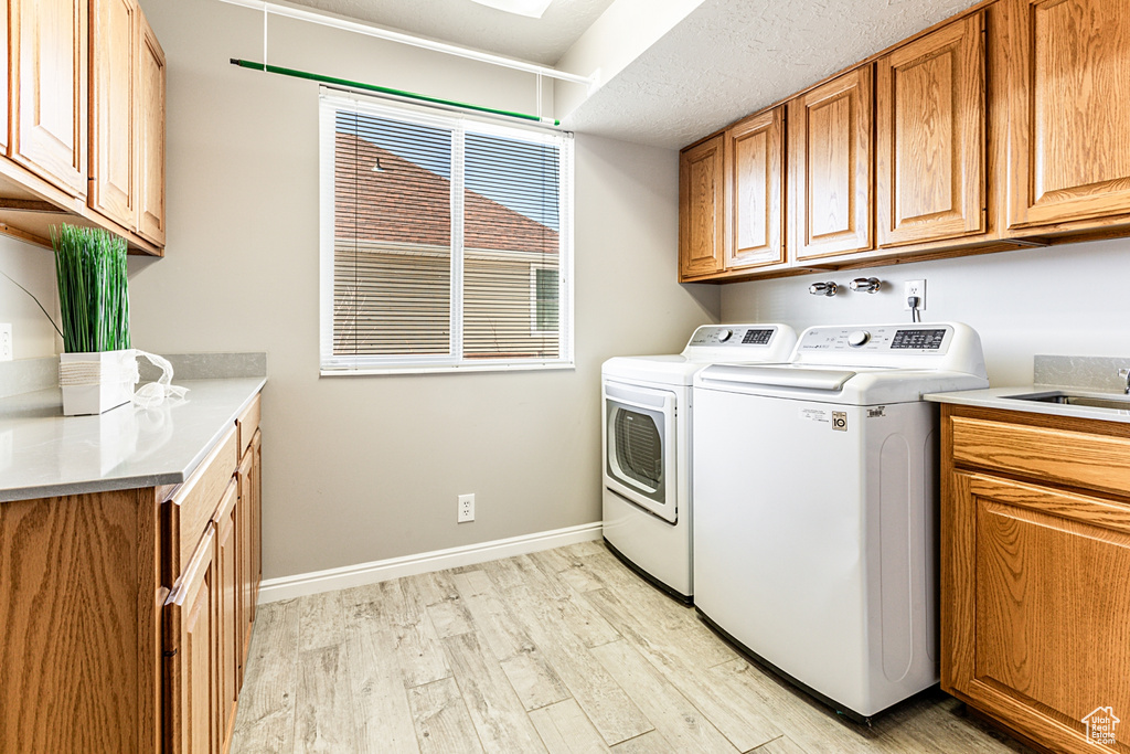 Laundry area with washing machine and clothes dryer, light hardwood / wood-style floors, cabinets, and a textured ceiling