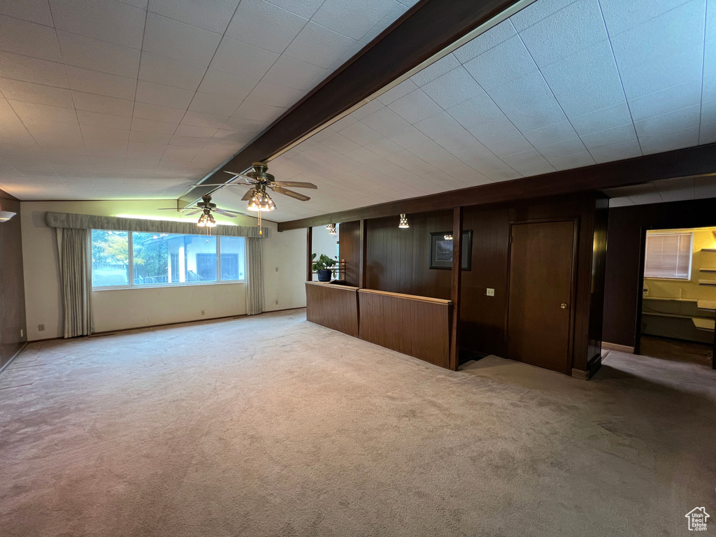 Carpeted empty room featuring ceiling fan and beam ceiling