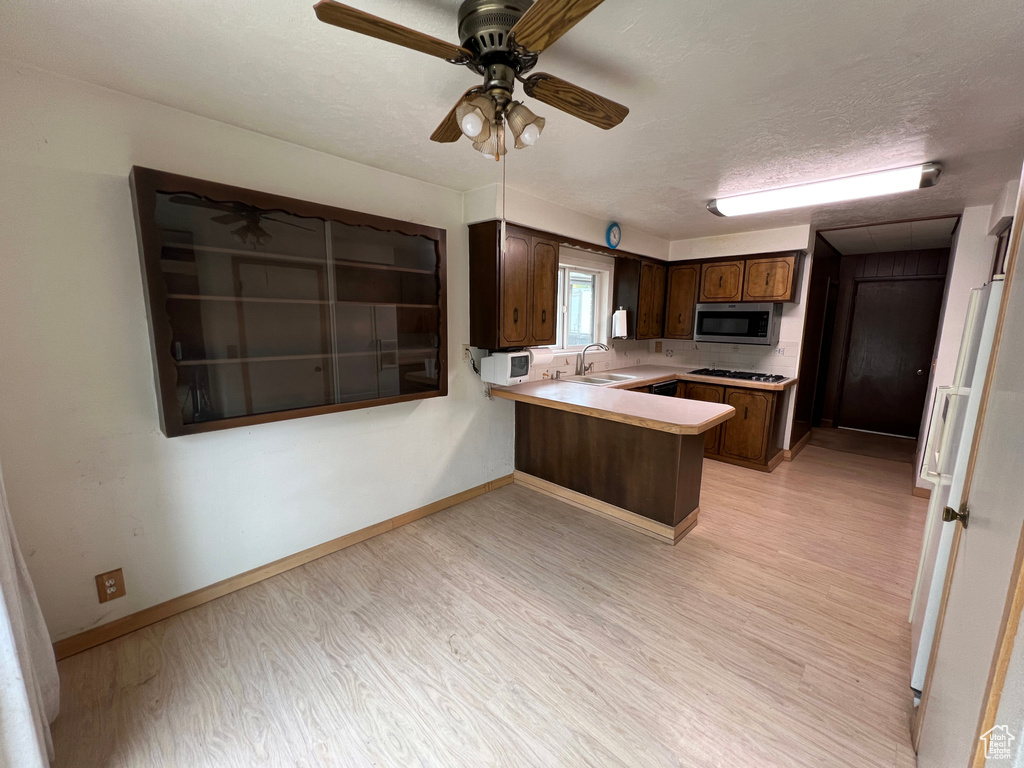 Kitchen featuring light hardwood / wood-style floors, gas stovetop, kitchen peninsula, ceiling fan, and sink