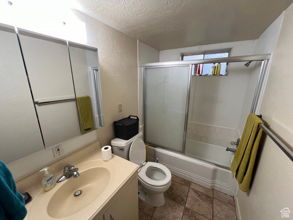 Full bathroom featuring vanity, a textured ceiling, tile flooring, bath / shower combo with glass door, and toilet