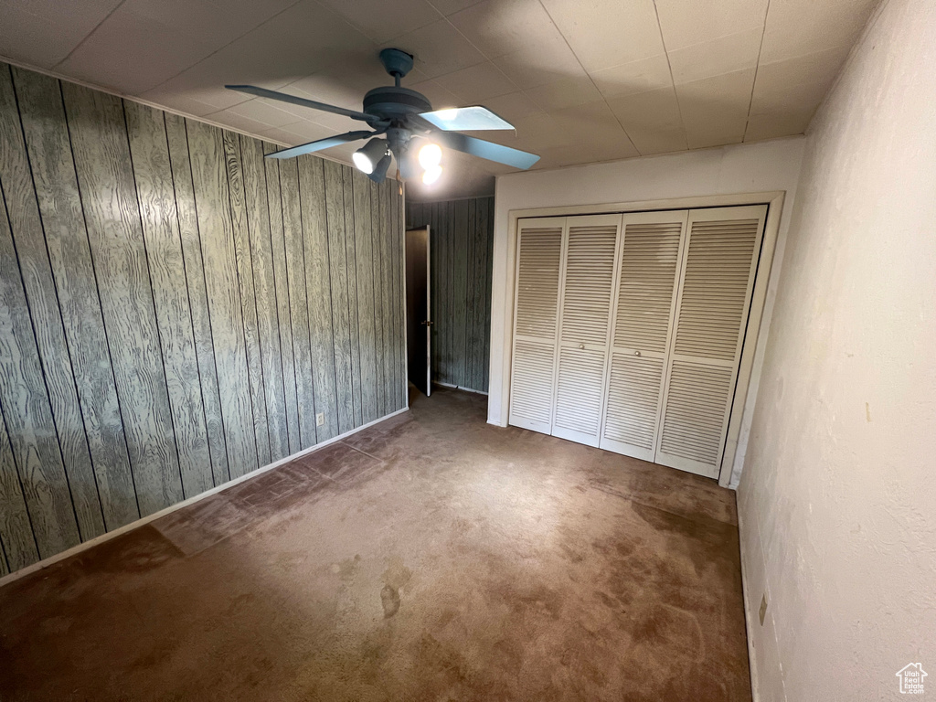 Unfurnished bedroom featuring ceiling fan, wooden walls, and a closet