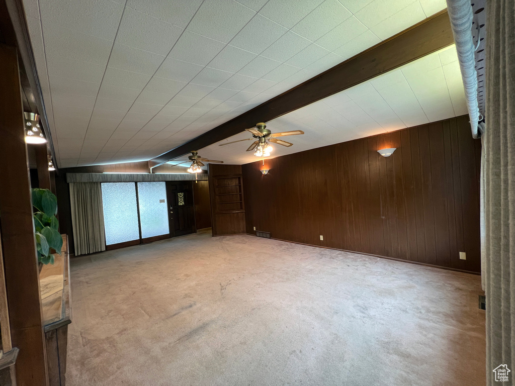 Unfurnished living room featuring ceiling fan, beamed ceiling, and wood walls