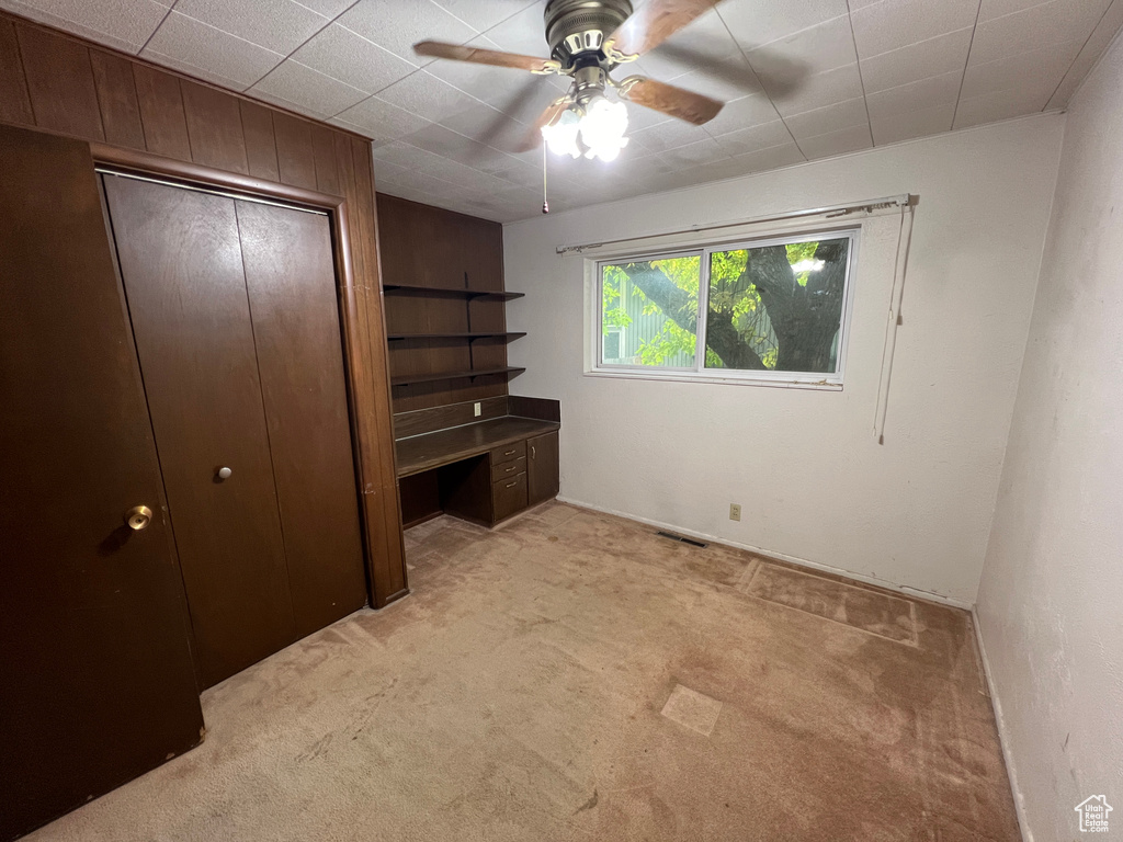 Unfurnished bedroom featuring ceiling fan, light carpet, wooden walls, and a closet