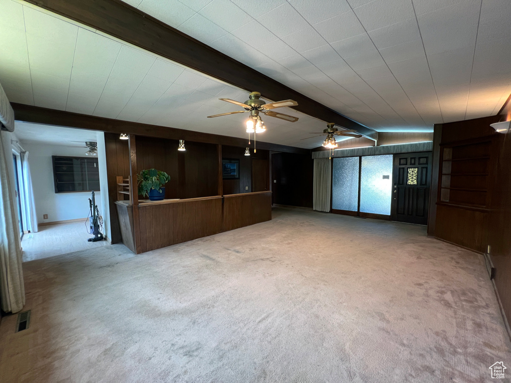 Interior space featuring ceiling fan, beam ceiling, light carpet, and wood walls