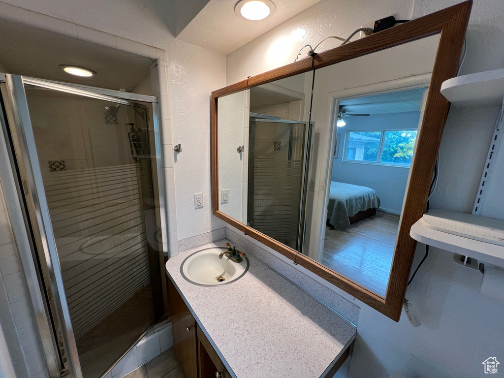 Bathroom featuring ceiling fan, oversized vanity, and an enclosed shower