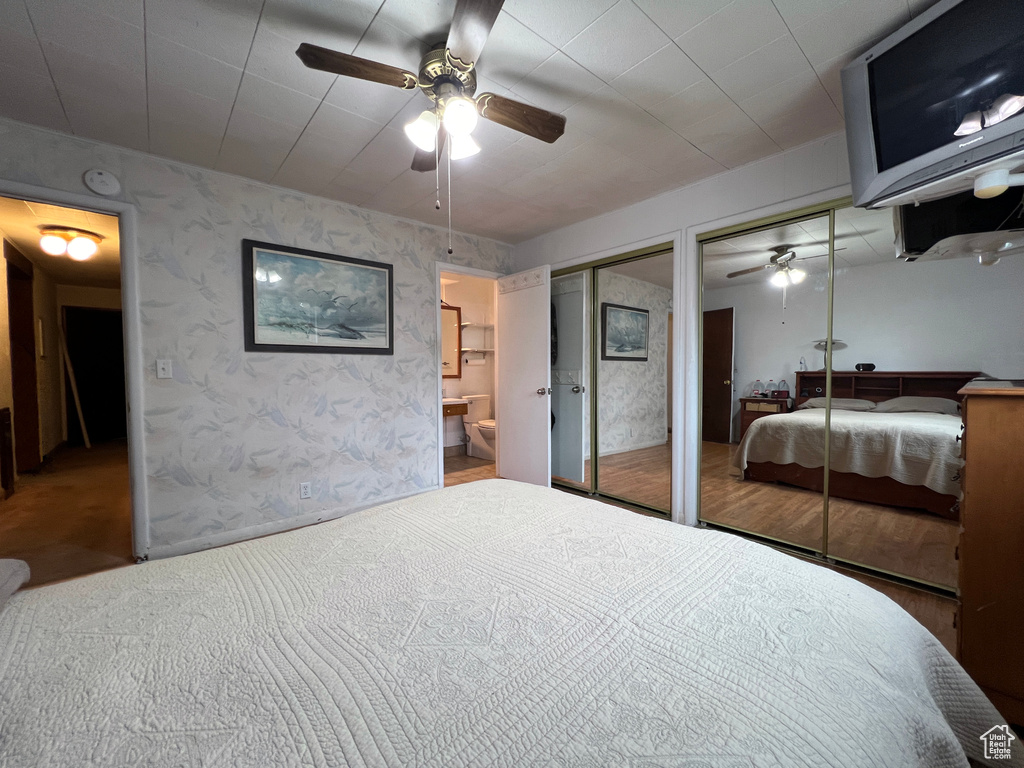 Carpeted bedroom featuring connected bathroom, ceiling fan, and two closets