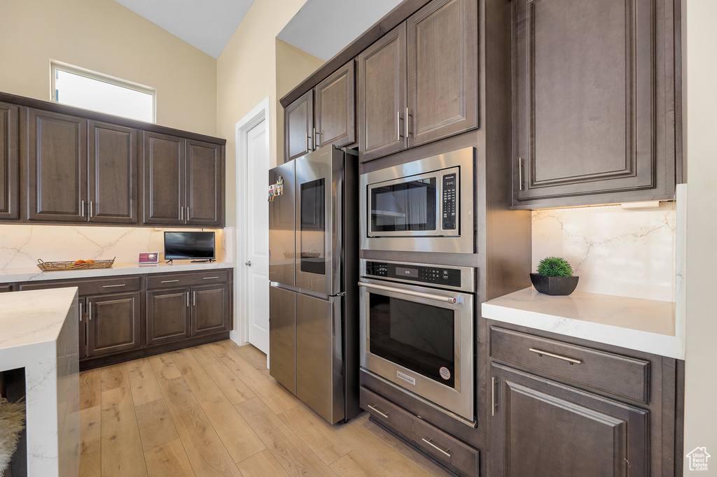 Kitchen with tasteful backsplash, dark brown cabinetry, appliances with stainless steel finishes, and light hardwood / wood-style flooring