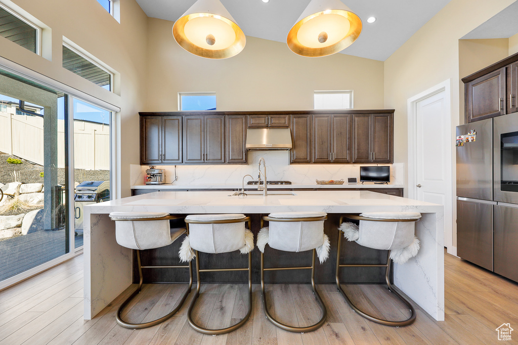 Kitchen with backsplash, light hardwood / wood-style flooring, dark brown cabinetry, and a kitchen island with sink
