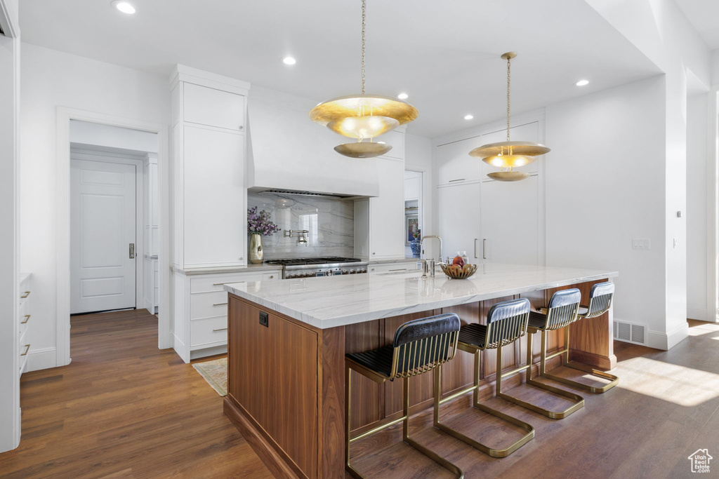 Kitchen featuring custom range hood, light hardwood / wood-style floors, decorative light fixtures, and white cabinetry