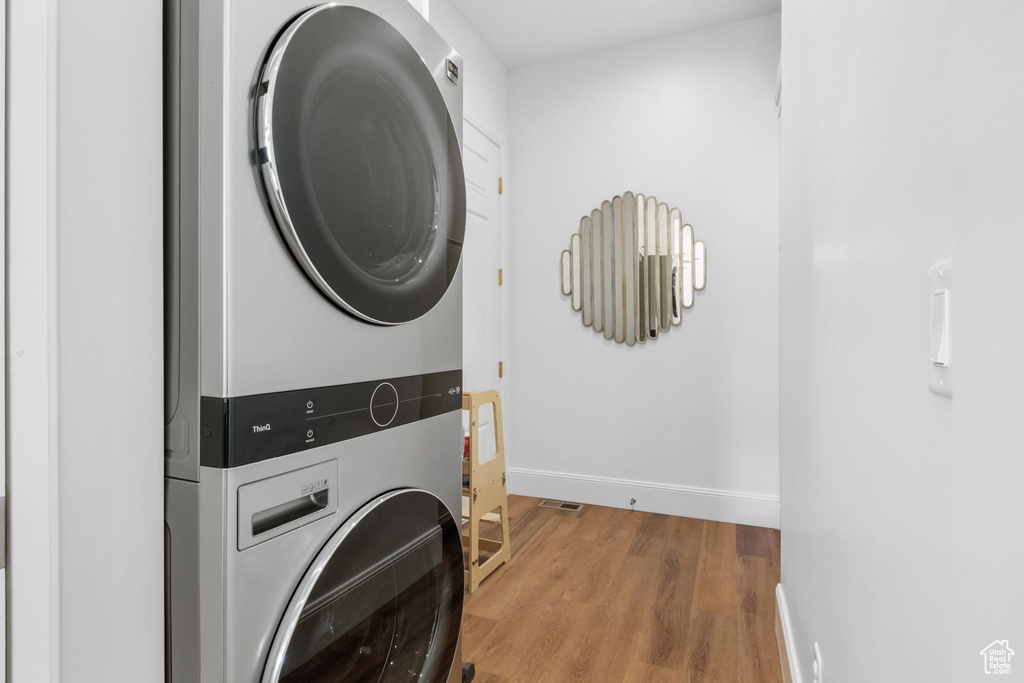 Laundry area with stacked washing maching and dryer and hardwood / wood-style floors