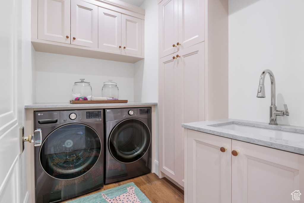 Laundry room with washing machine and clothes dryer, light hardwood / wood-style floors, cabinets, and sink