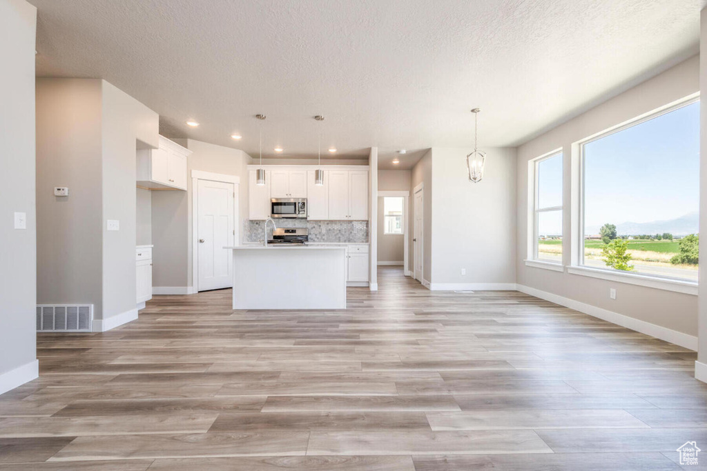 Kitchen featuring hanging light fixtures, white cabinets, a center island, tasteful backsplash, and light wood-type flooring