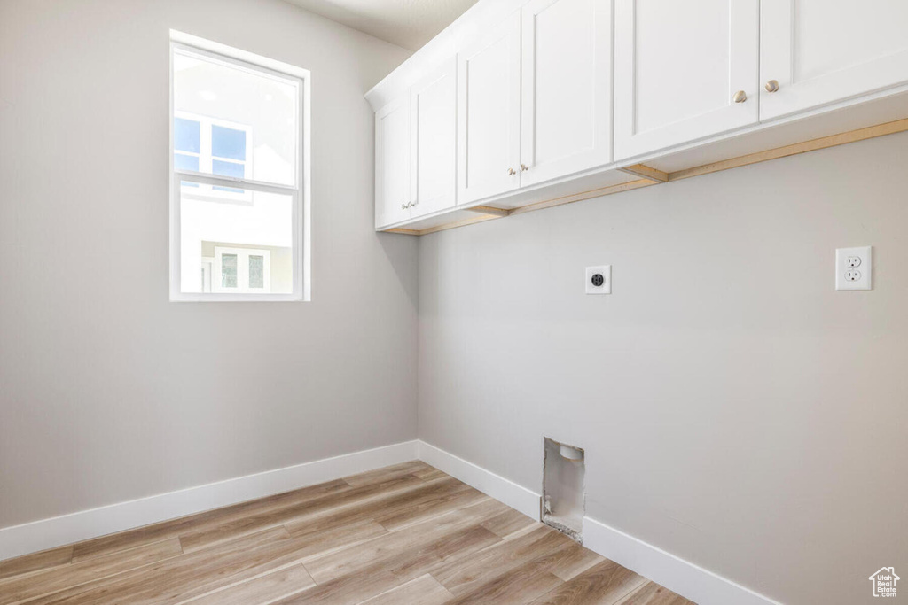 Clothes washing area with cabinets, hookup for an electric dryer, and light hardwood / wood-style floors