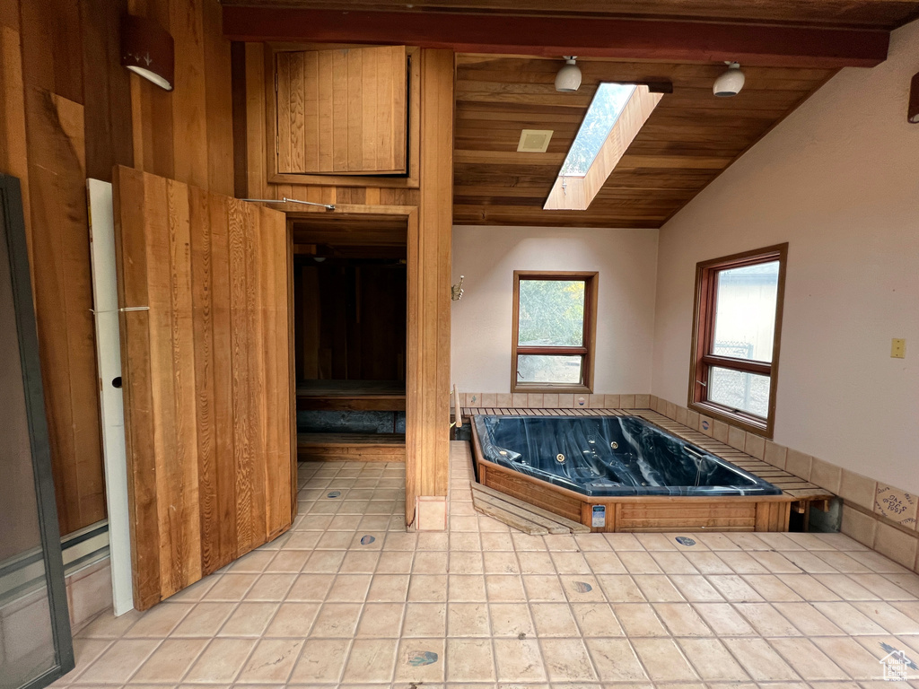 Bathroom with lofted ceiling with skylight, wooden ceiling, a bath, and tile flooring