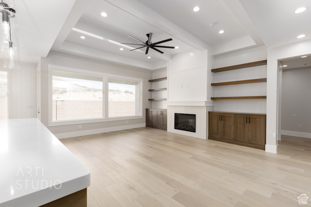 Unfurnished living room with ceiling fan, a tray ceiling, and light wood-type flooring