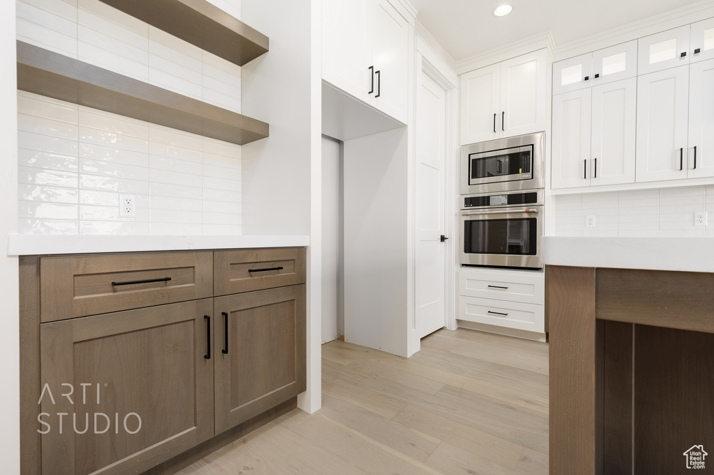 Kitchen with appliances with stainless steel finishes, light wood-type flooring, backsplash, and white cabinetry