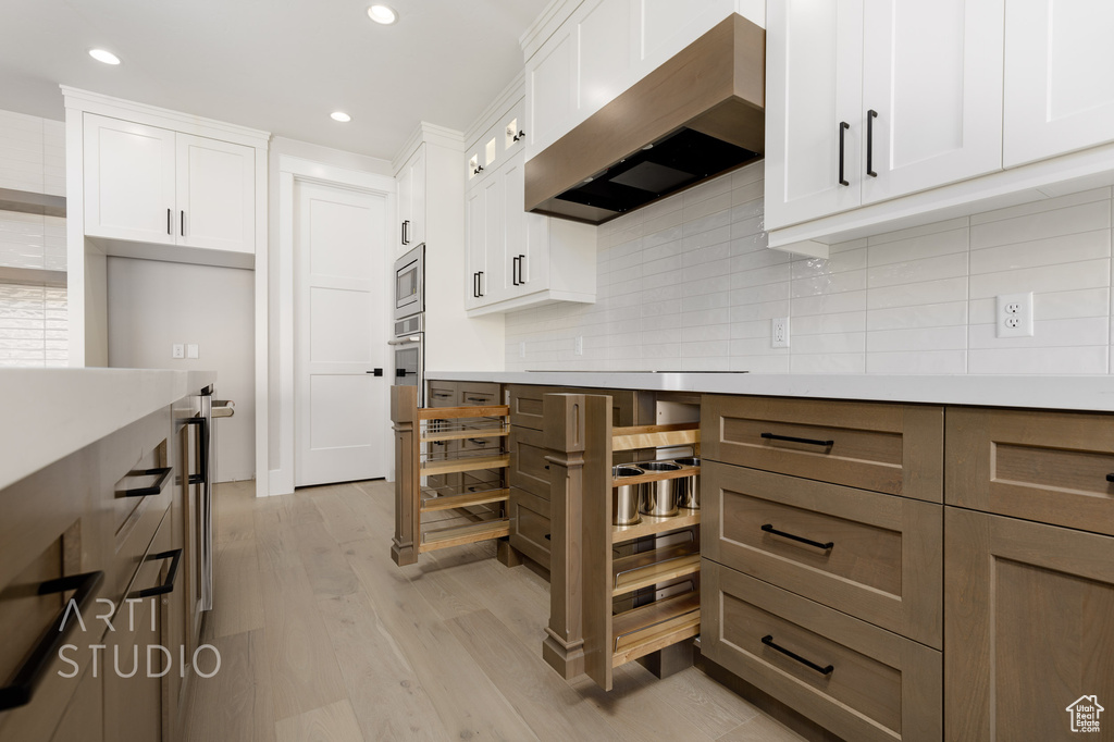 Kitchen featuring white cabinets, tasteful backsplash, light hardwood / wood-style floors, and wall chimney range hood